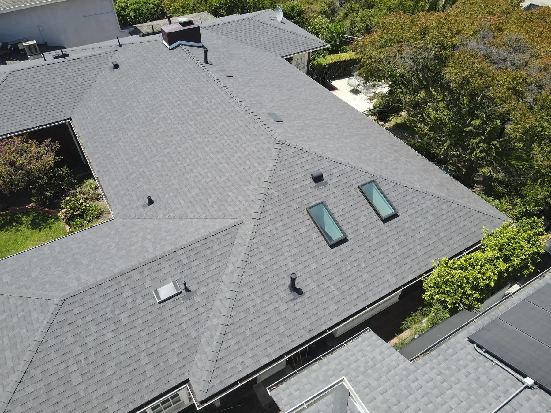Angled view along the roof, with the new shingles, hips and ridges running clean and three skylights set into the roof