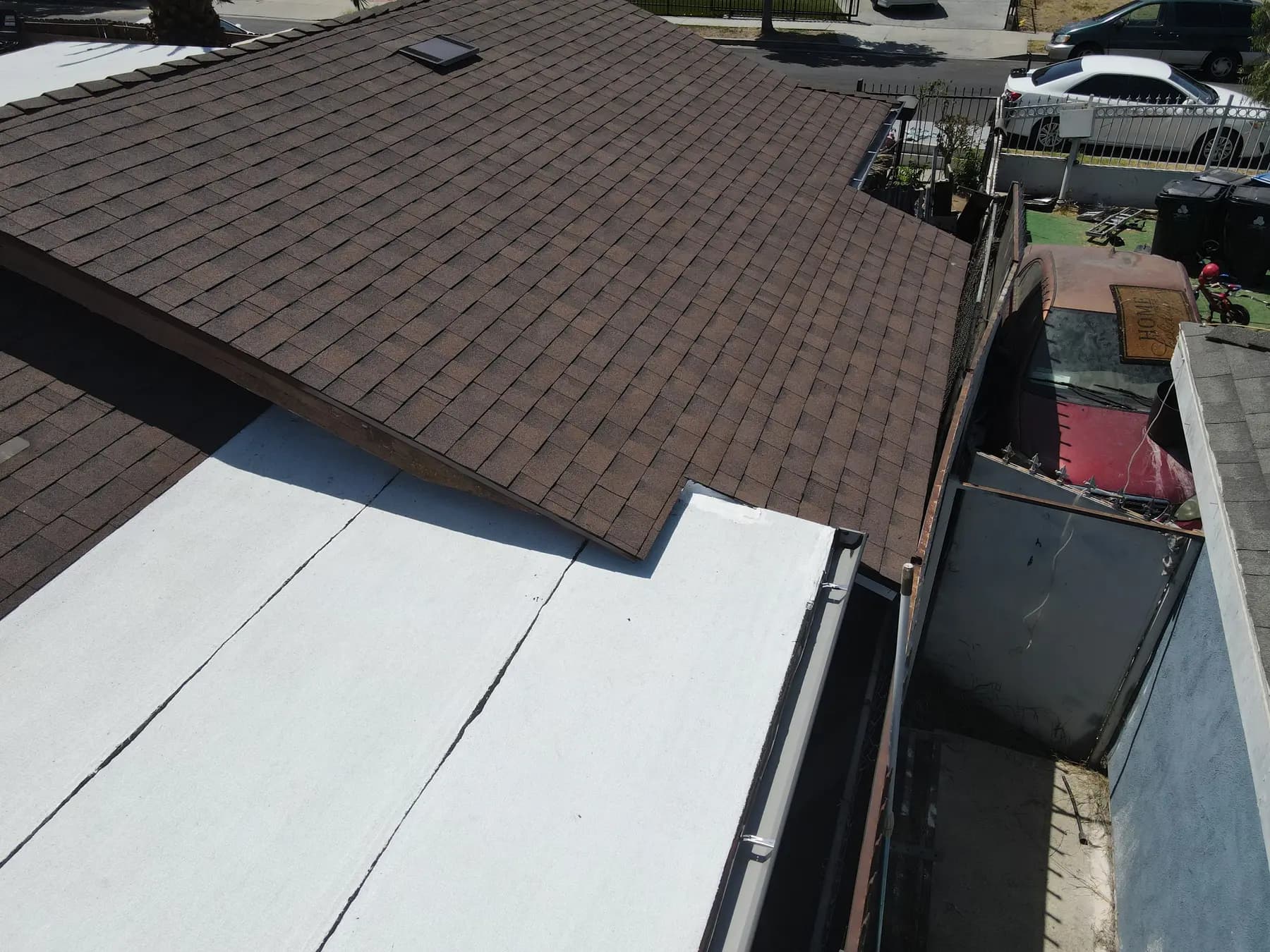 Close view of the white flat roof section meeting the new brown shingle roof, with its edge and wall transition finished