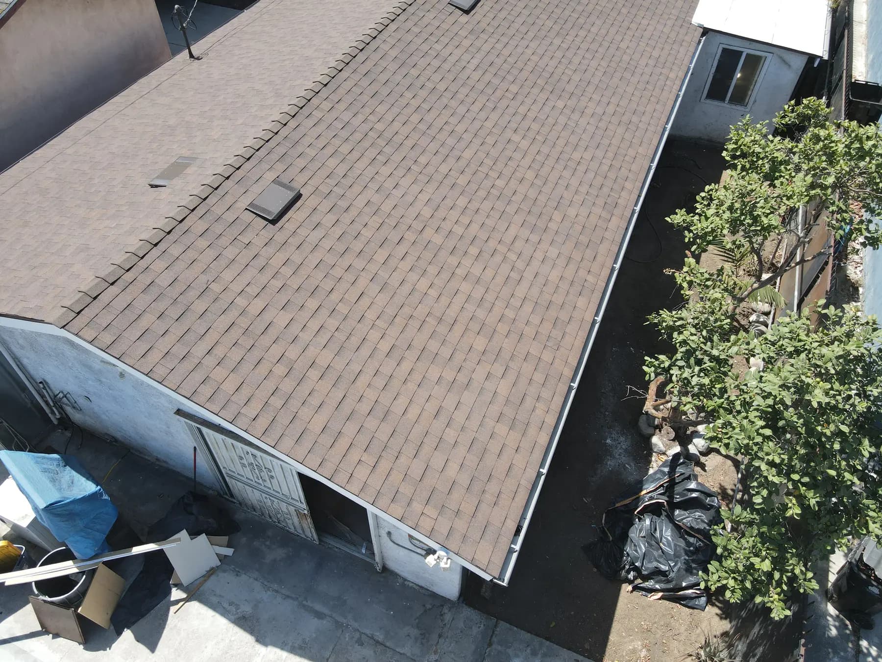 Long new brown shingle roof on the rear building, with box vents along the slope and a clean ridge