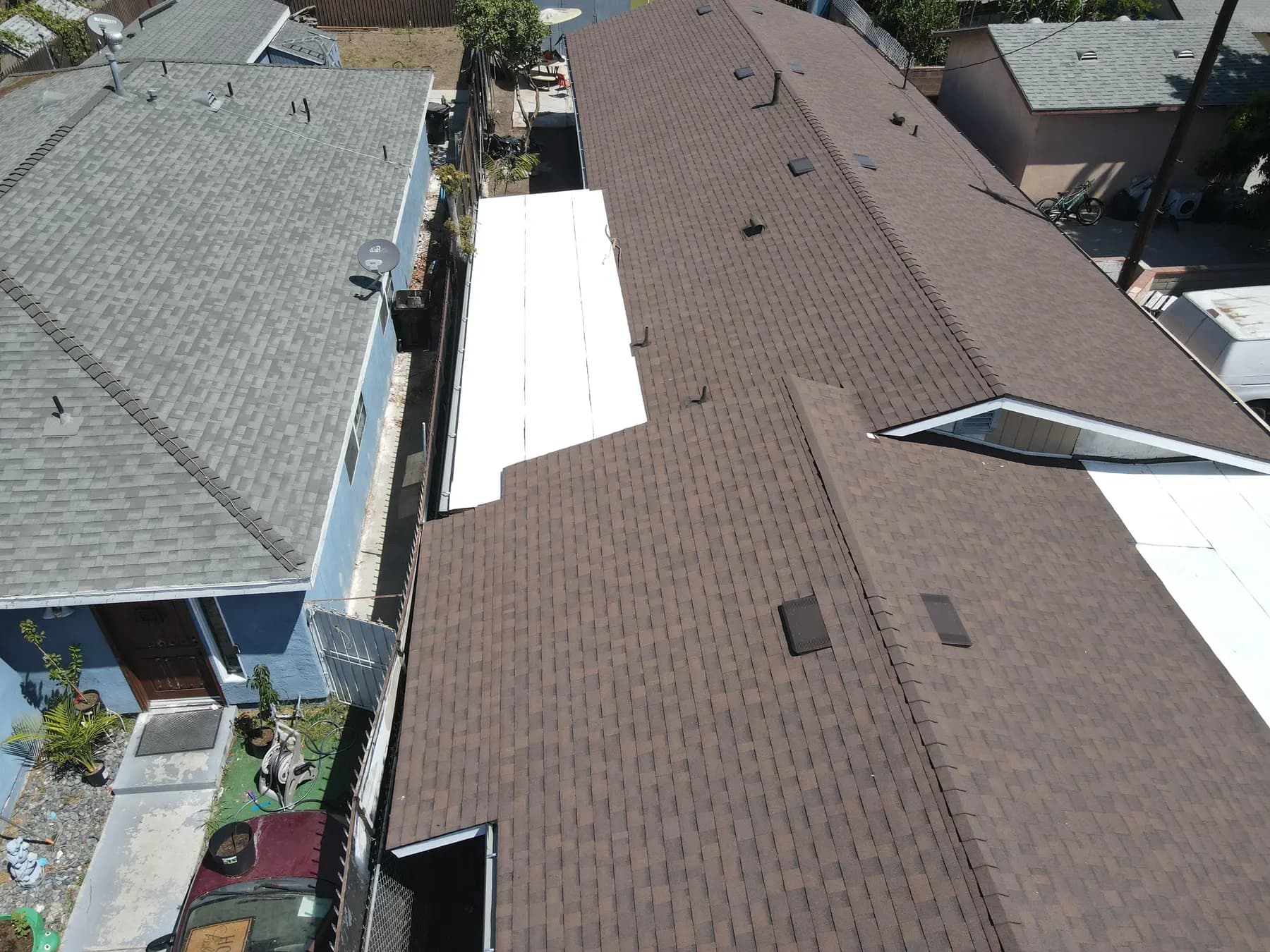 The long home from above, with new brown shingles, gabled vent openings and a white flat section at the side