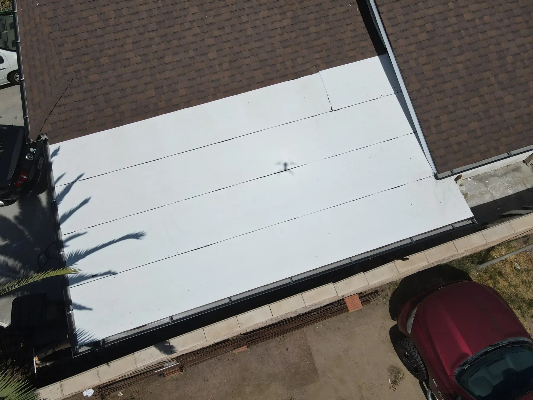 White flat roof section beside the new shingle roof, with clean seams and a finished edge along the driveway
