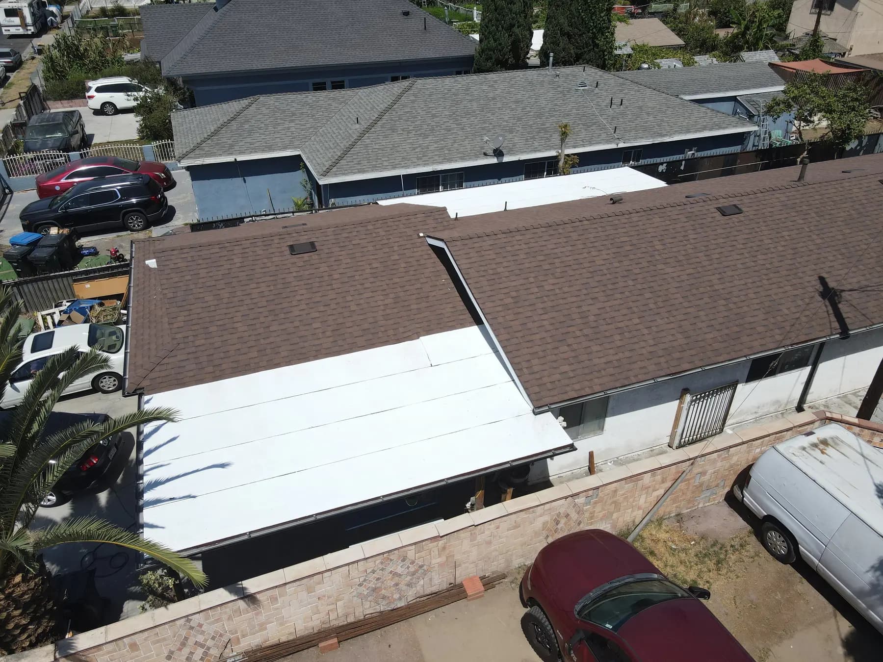 A white flat roof section beside the new brown shingle roof on the front of the property
