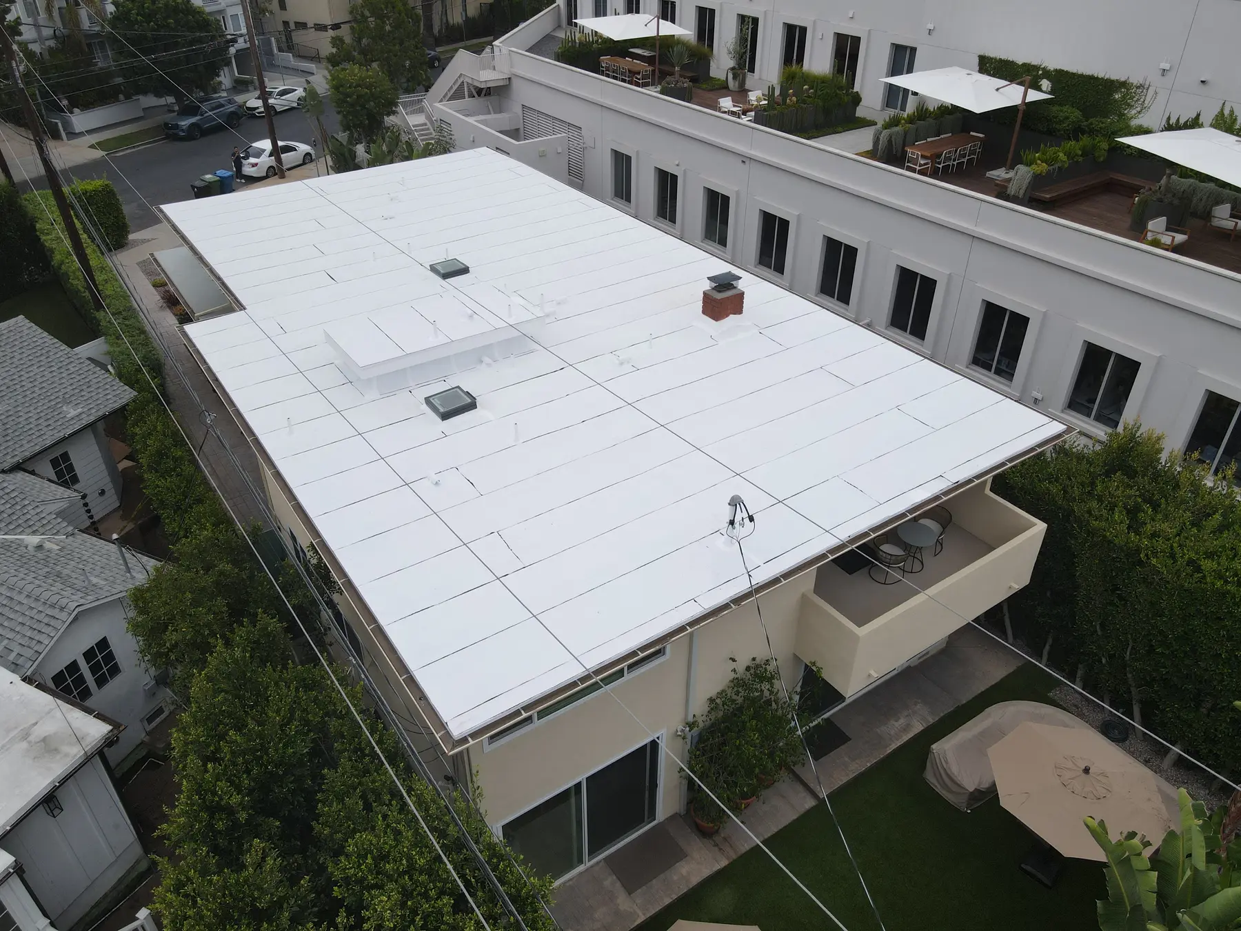 Aerial view of the new white flat roof on a two-story mid-century home in Los Angeles, with its skylights, brick chimney and raised window box
