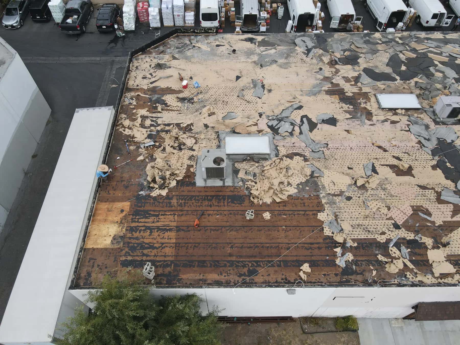 Close view of the stripped roof: the bare plank deck, a new sheet of plywood in the corner and piles of torn base sheet by the AC unit