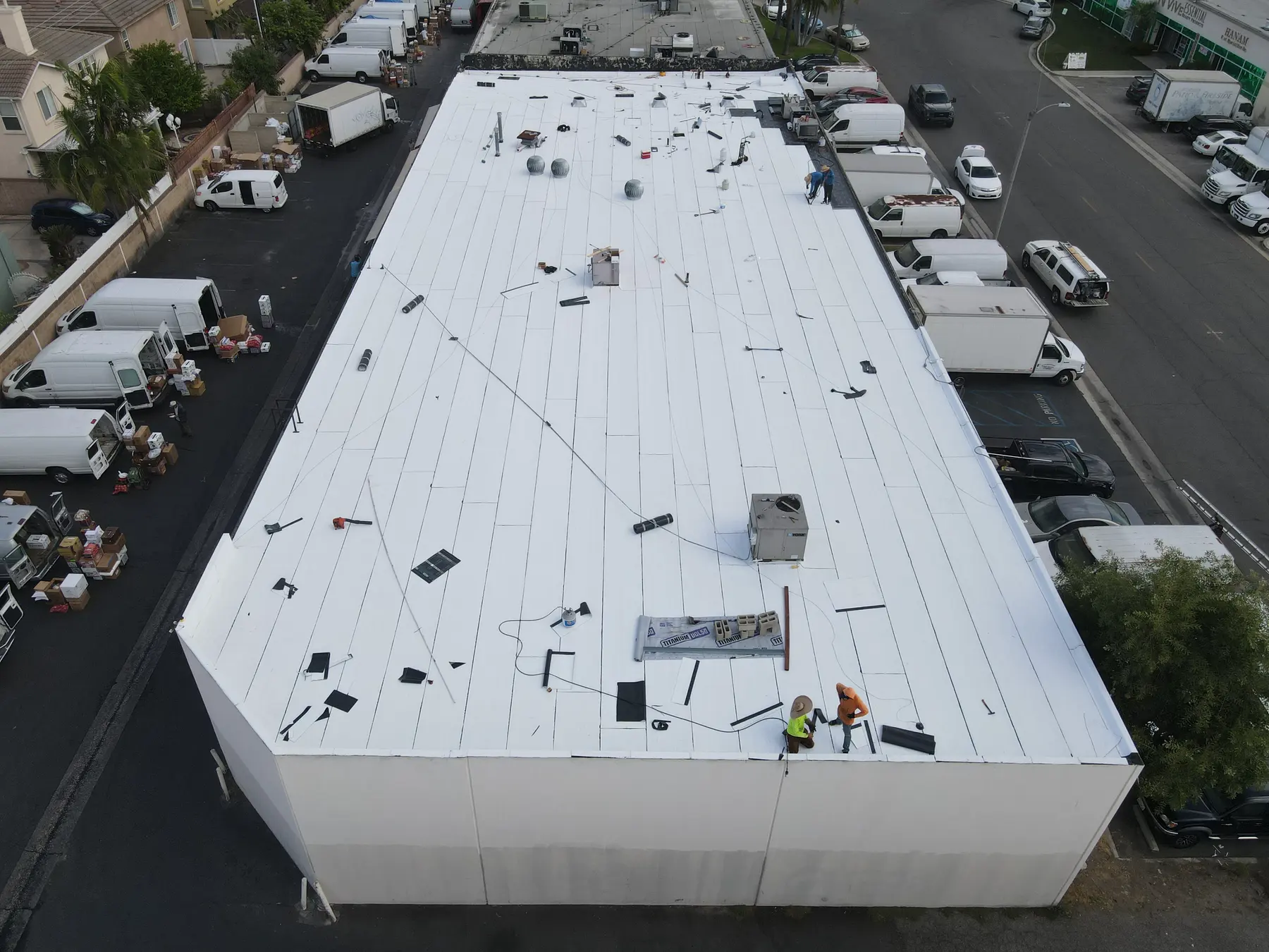 The building from the same spot as on the tear-off day, now under the new white cap sheet, with roofers at the far corner