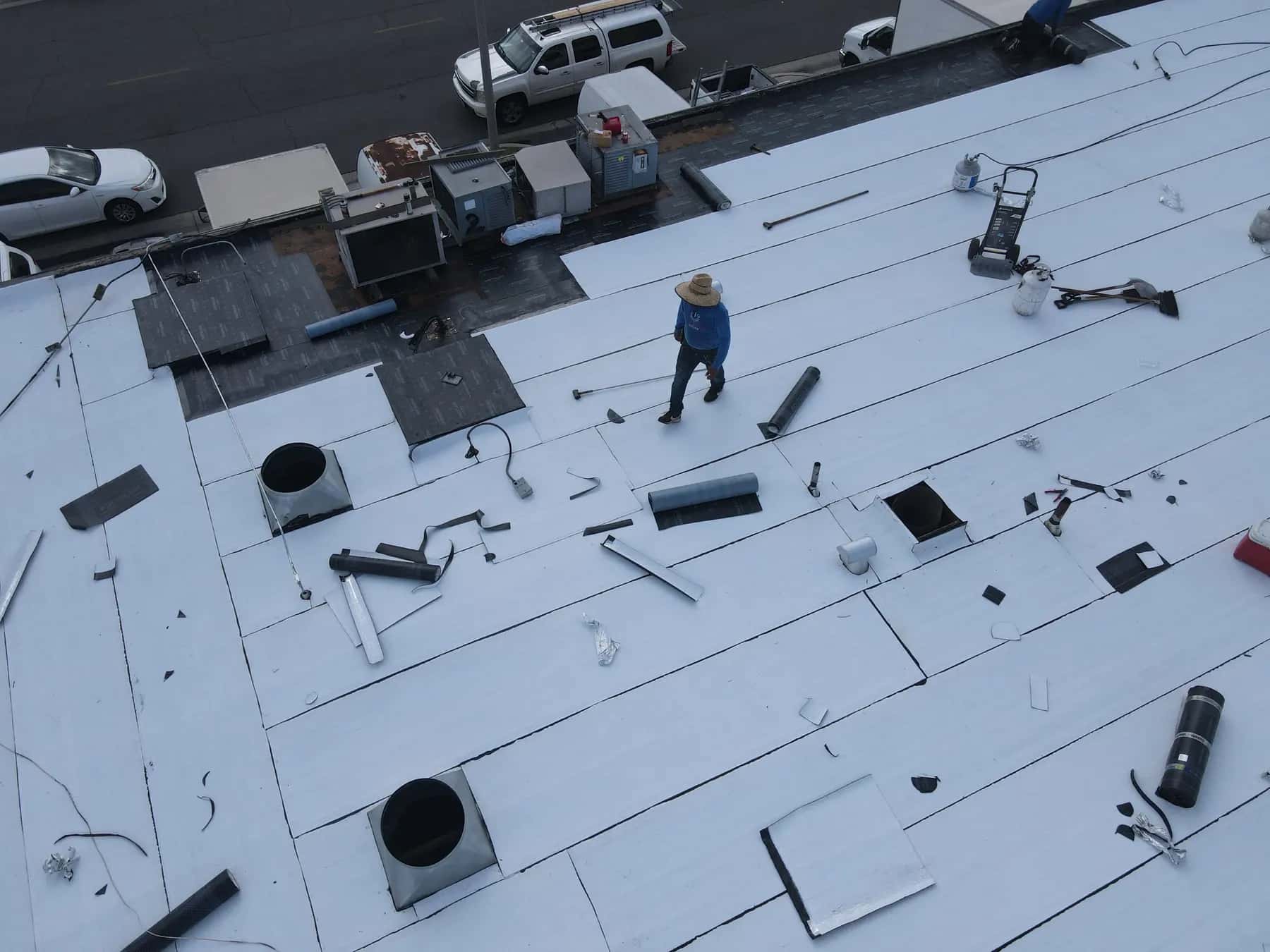 A roofer walking the new cap sheet, with the exhaust curbs flashed and the black base sheet still showing along the front by the rooftop units