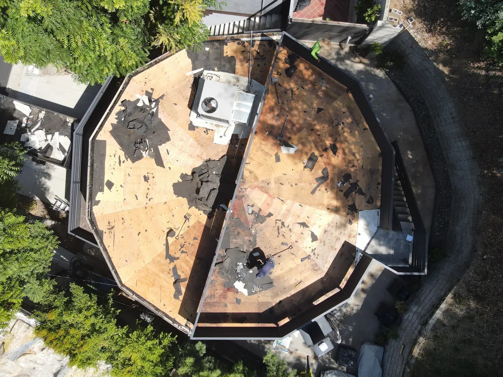 Top-down view of the round roof stripped to the deck, split by the rooftop deck railing