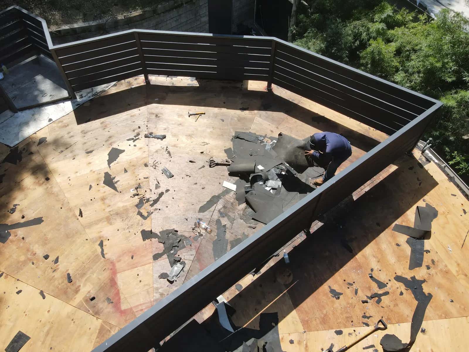 Roofer clearing old roofing from the deck along the rooftop railing