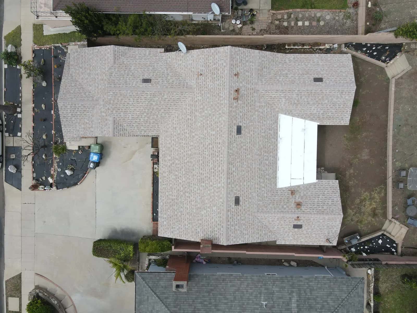 Overhead drone view of the finished roof, with warm tan architectural shingles across the hips and valleys and the white flat patio cover