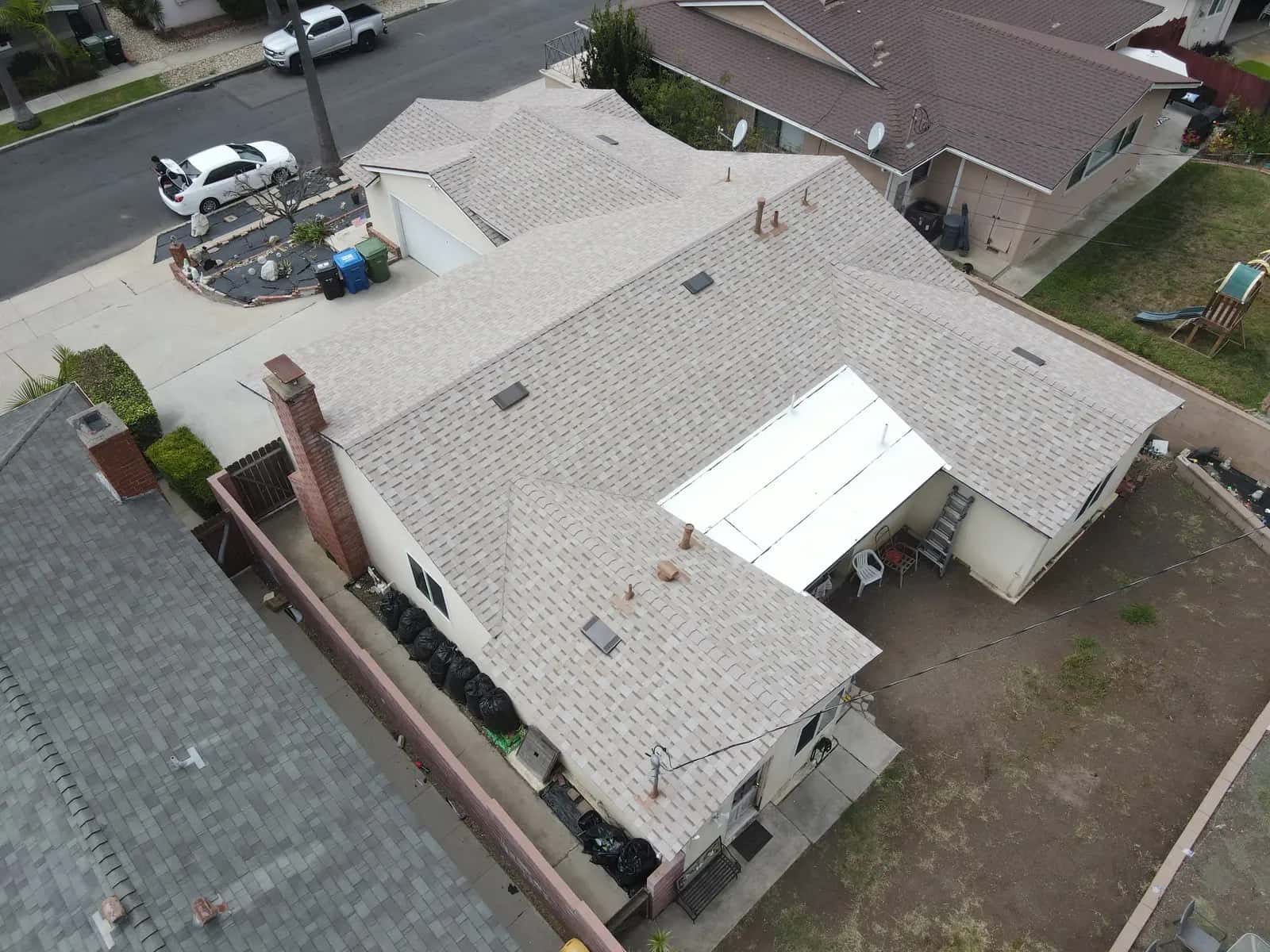 New shingle roof and white patio cover beside a brick chimney