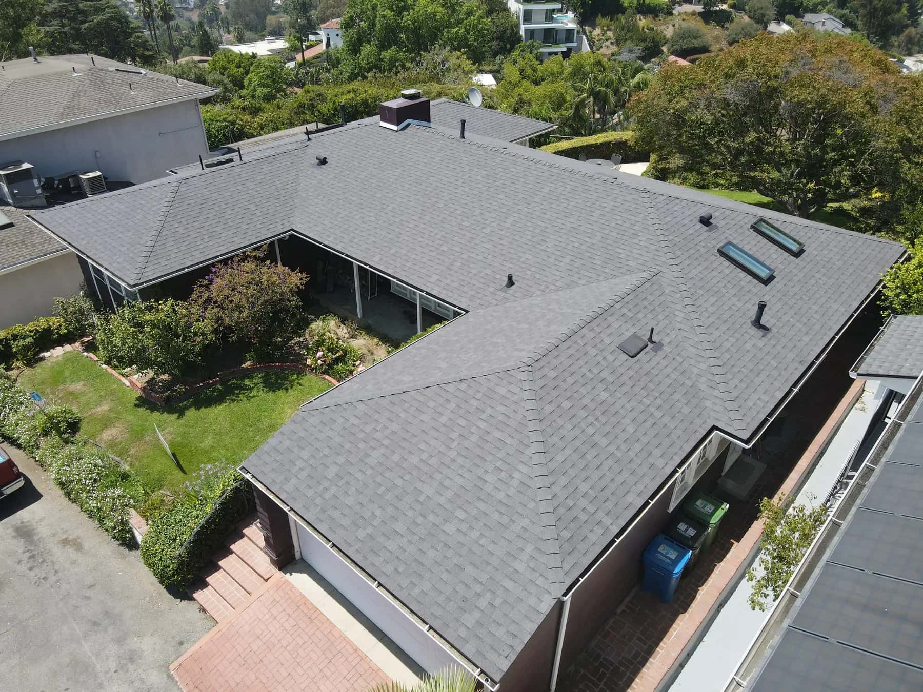 Aerial view of a single-story home in Granada Hills with a new gray shingle roof wrapped around a garden, with a brick chimney and two skylights