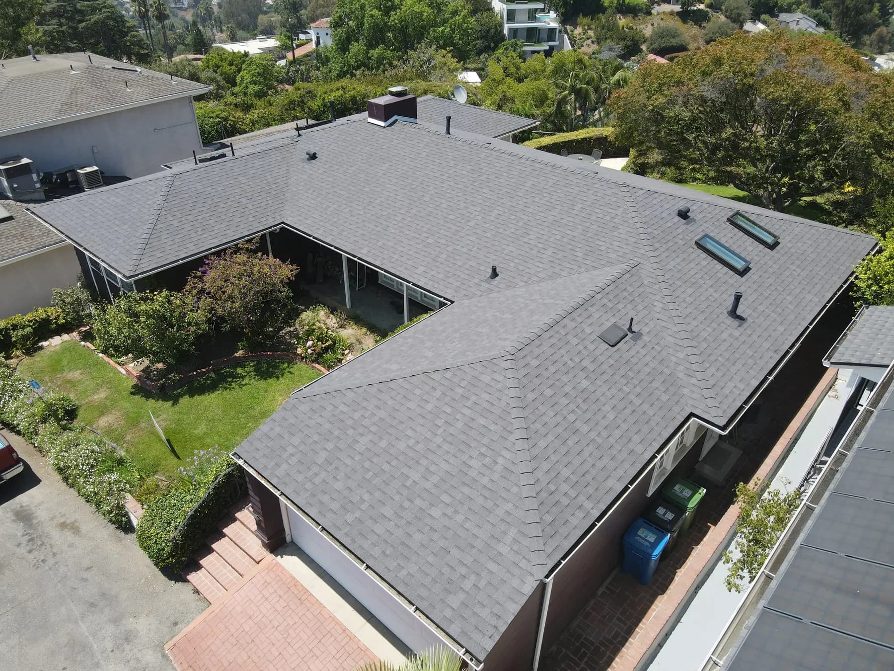 Aerial view of a single-story home in Granada Hills with a new gray shingle roof wrapped around a garden, with a brick chimney and two skylights