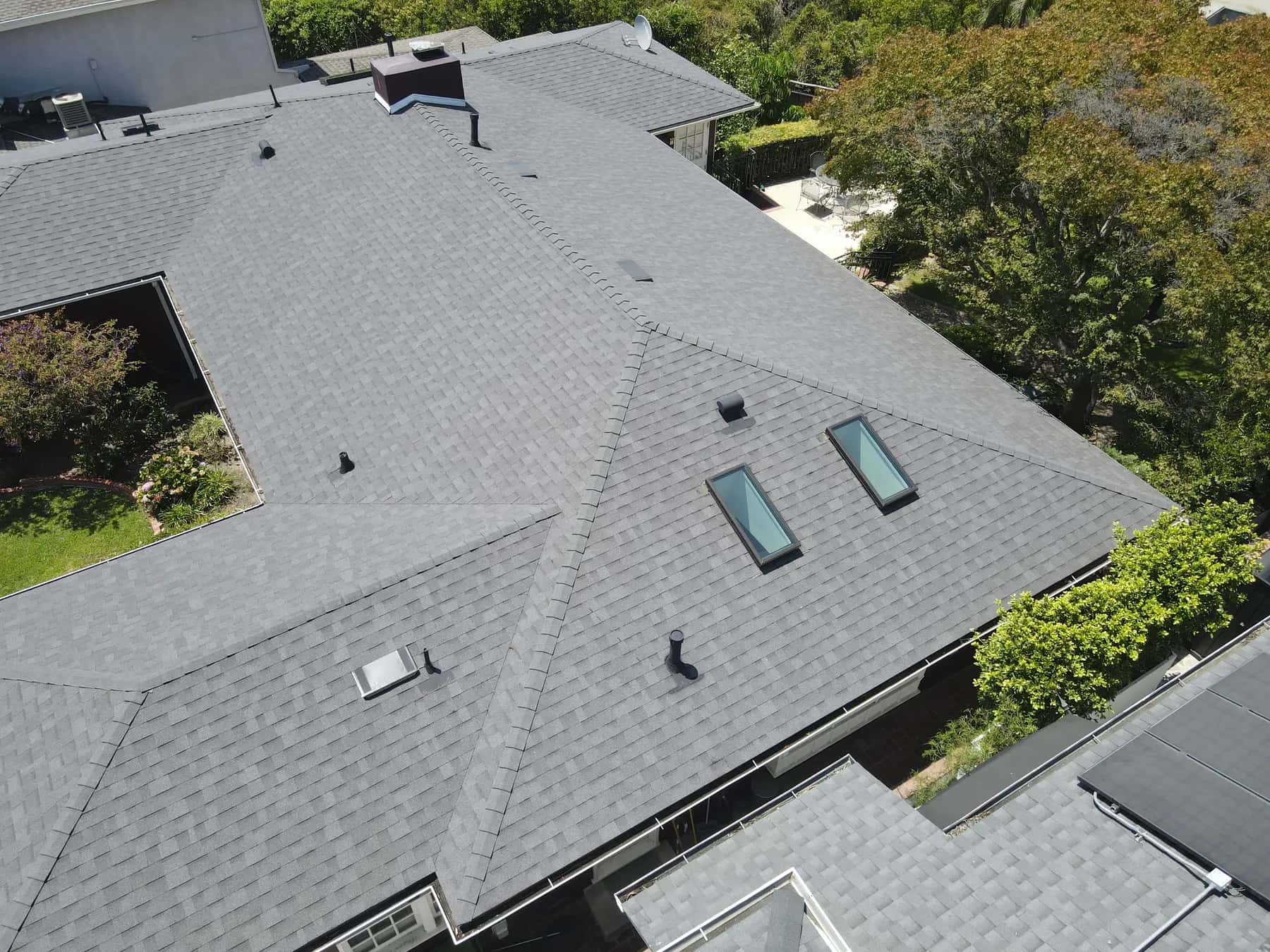 Angled view along the roof, with the new shingles, hips and ridges running clean and three skylights set into the roof