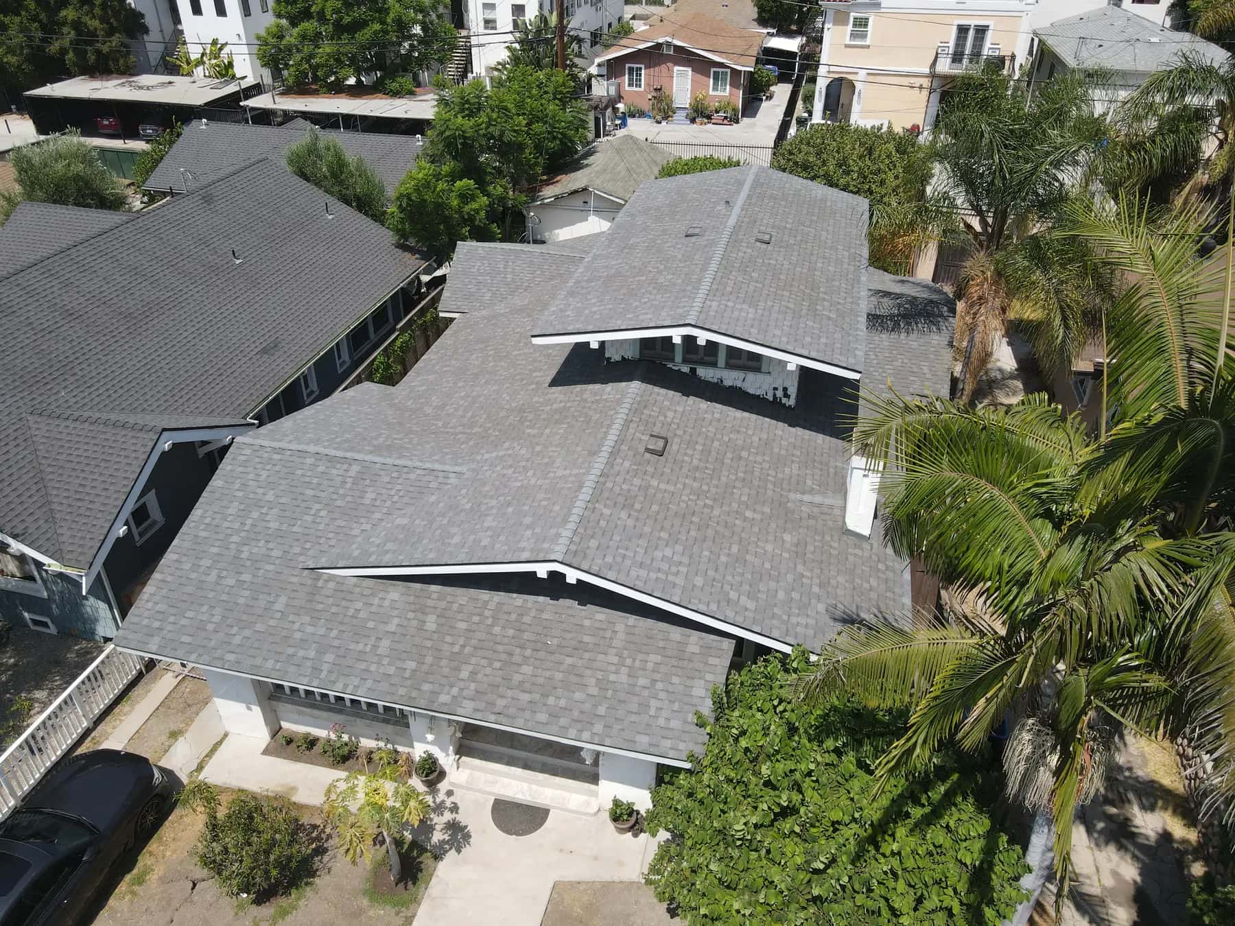 Aerial view of a Craftsman-style home in Westlake with a new gray shingle roof of many gables, a white chimney and palm trees beside it