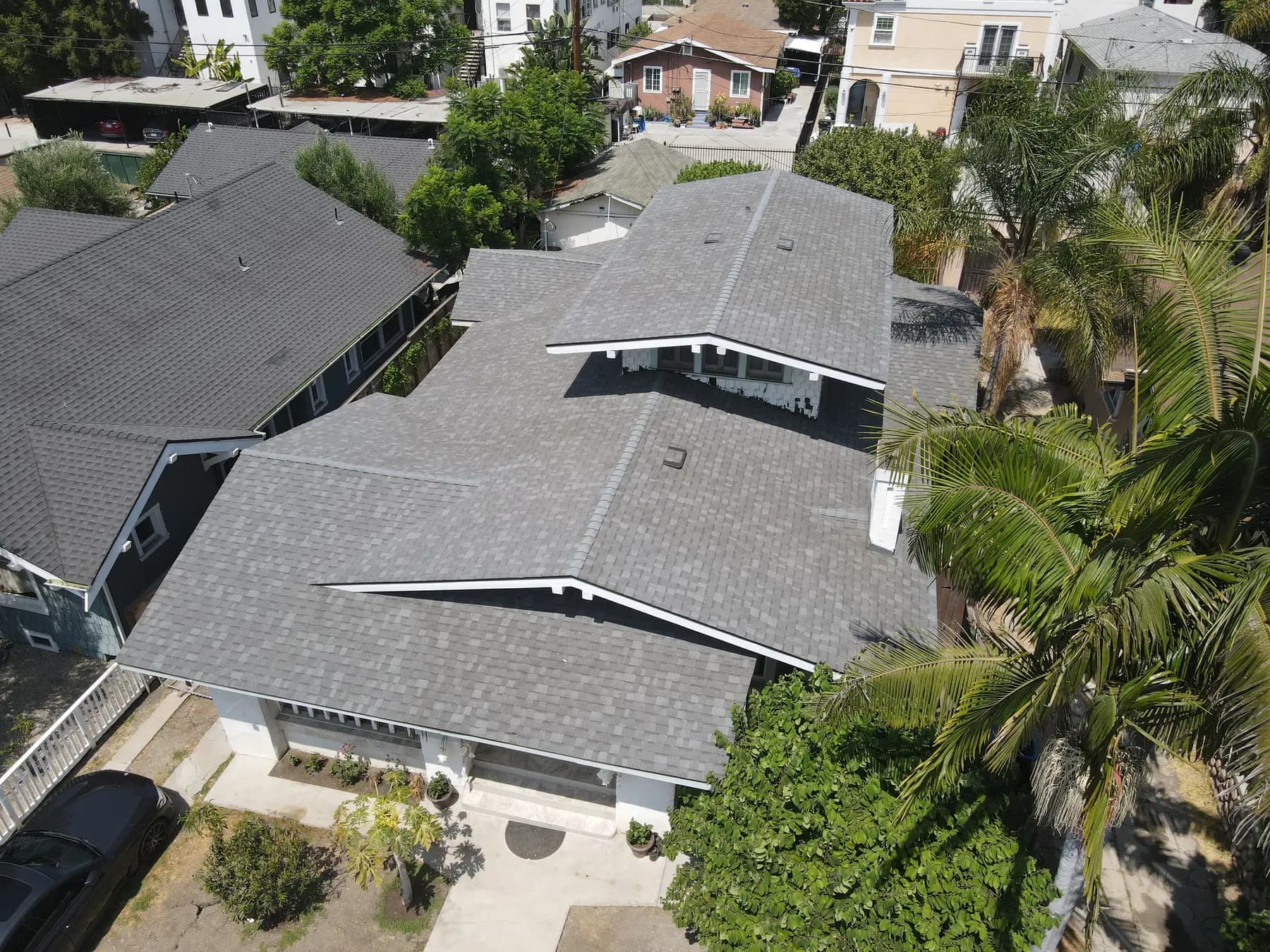 Aerial view of a Craftsman-style home in Westlake with a new gray shingle roof of many gables, a white chimney and palm trees beside it
