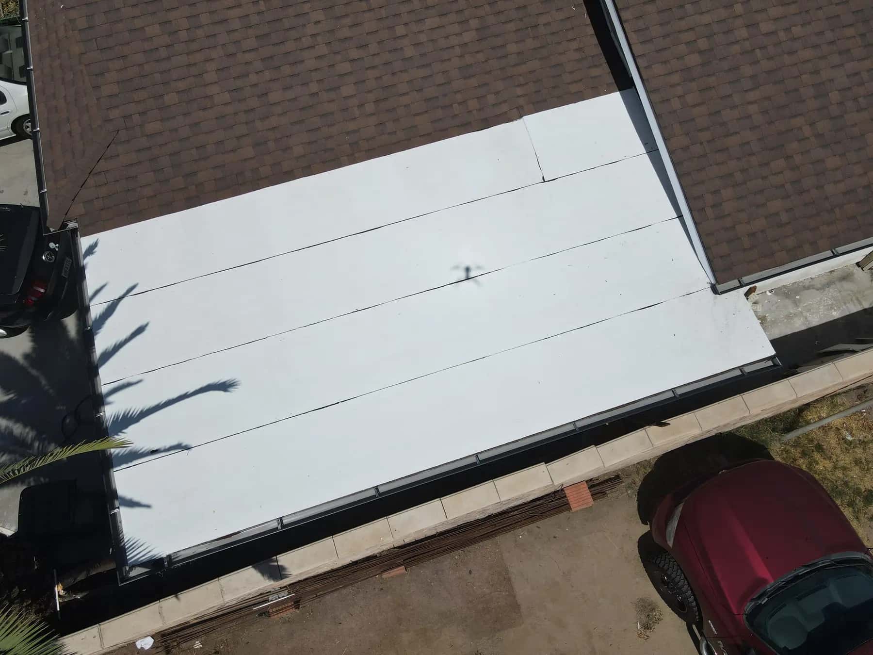White flat roof section beside the new shingle roof, with clean seams and a finished edge along the driveway