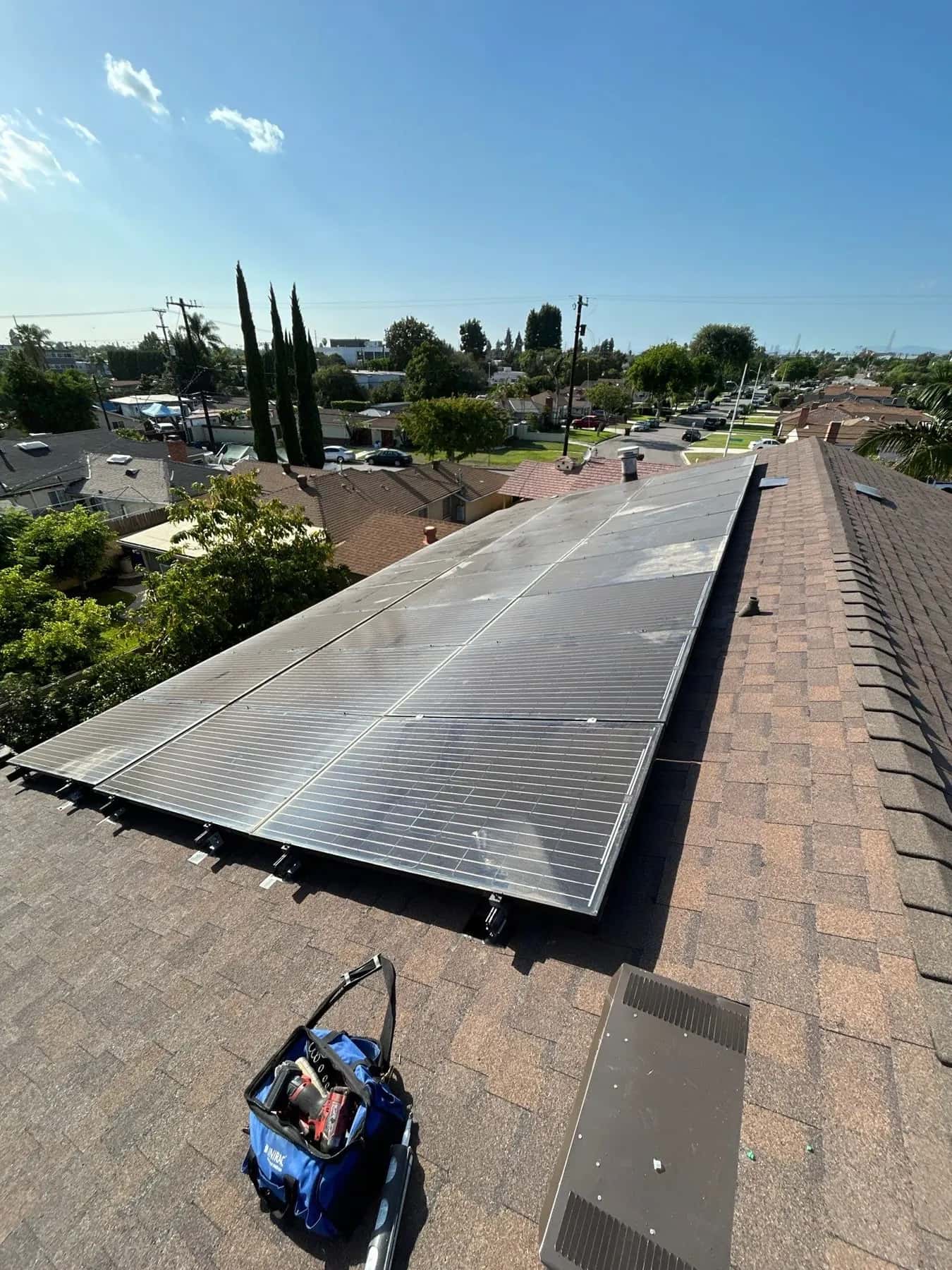 The solar array back on the new brown shingle roof of a home in Pico Rivera, with the neighborhood behind it