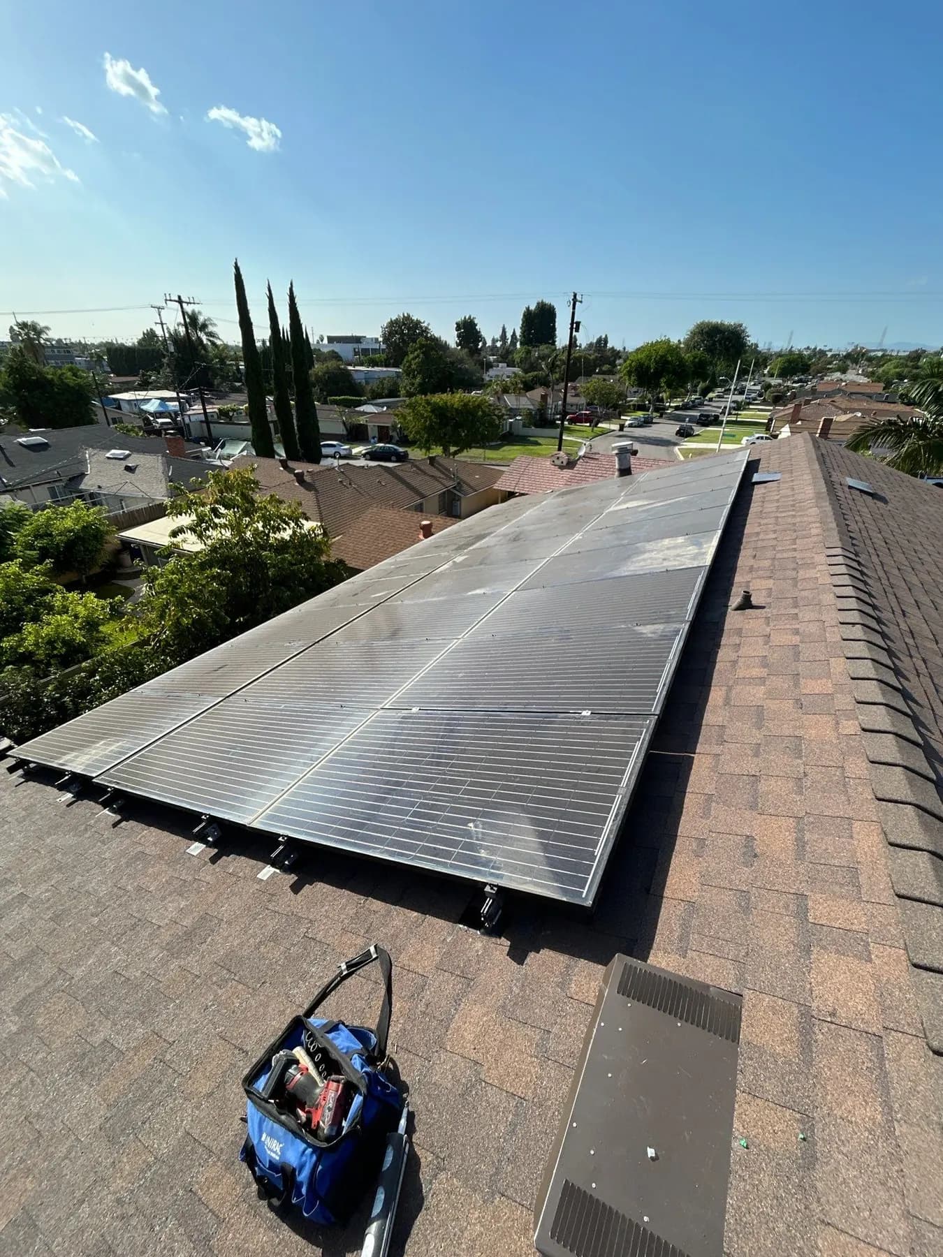 The solar array back on the new brown shingle roof of a home in Pico Rivera, with the neighborhood behind it
