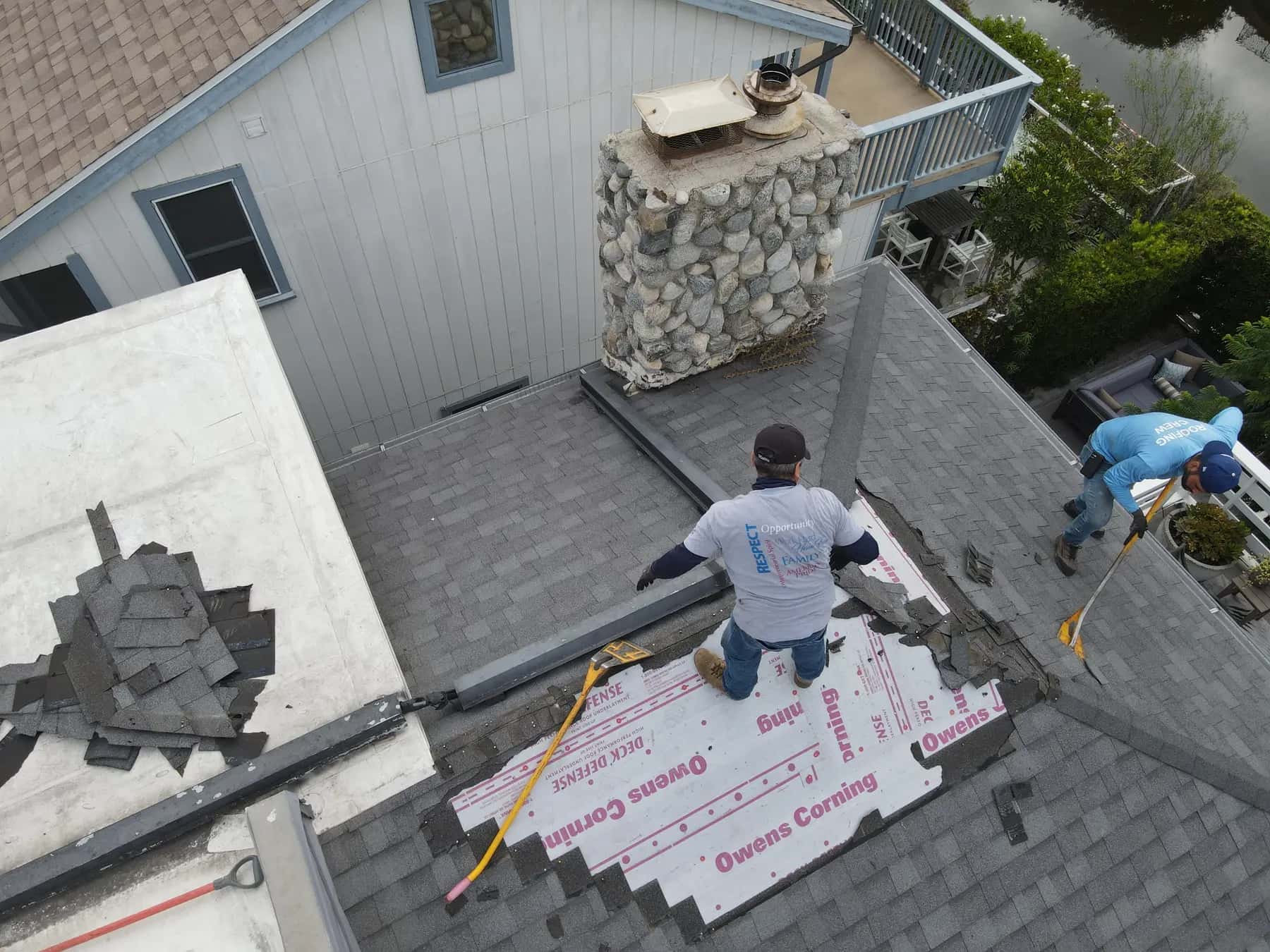 Roofers tearing off the old shingles and laying Owens Corning underlayment over the exposed roof deck