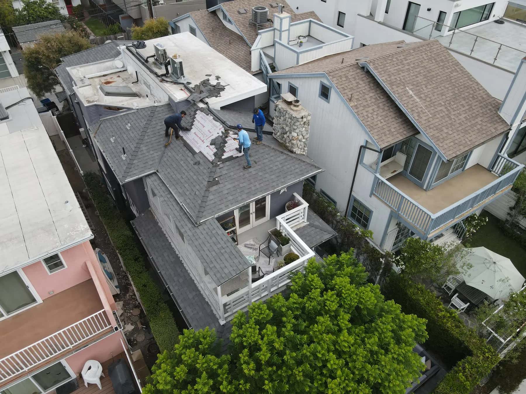 The tear-off moving across the main hip roof, with a roofer at each side of the exposed section