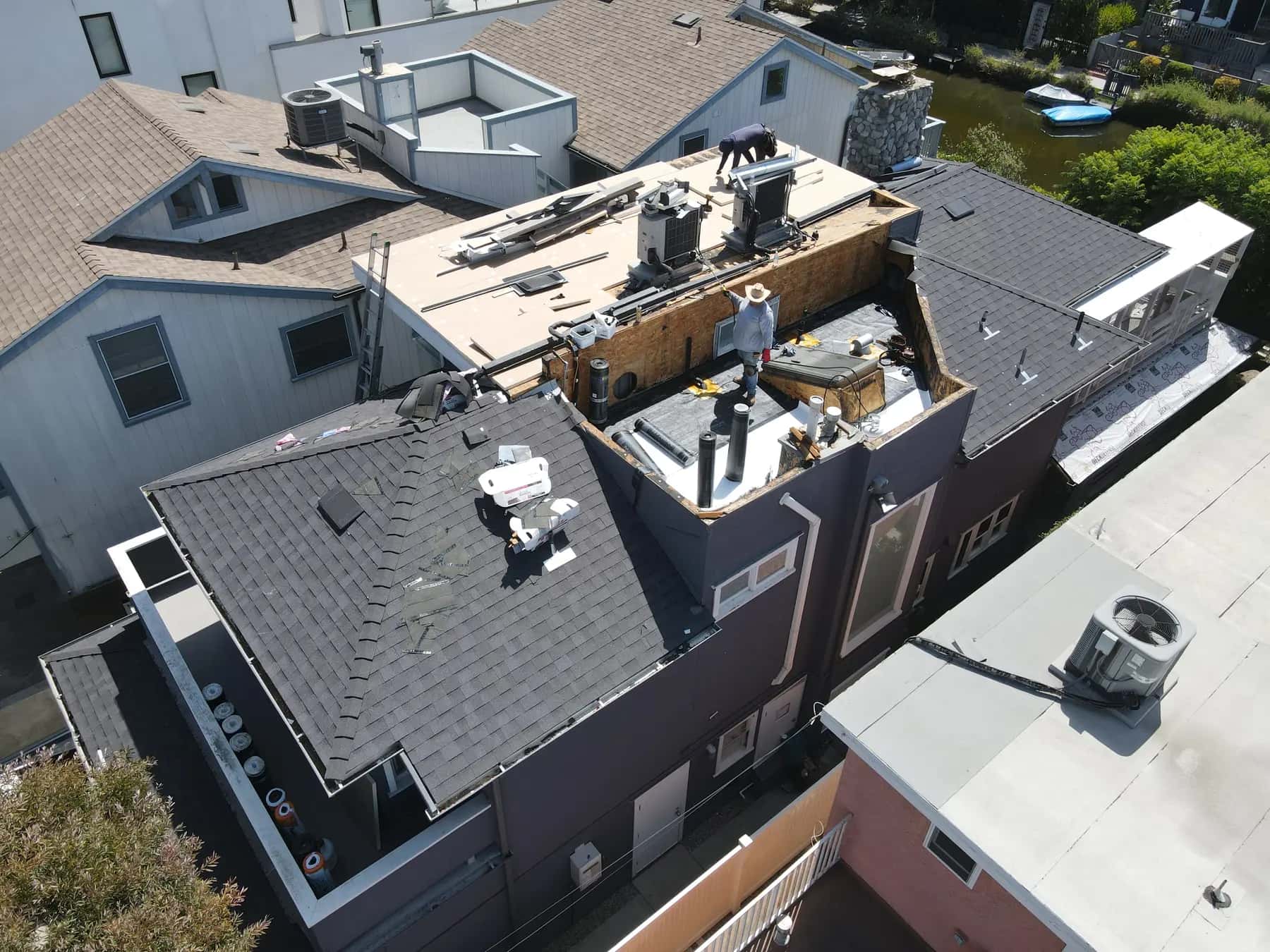New charcoal shingles finished on the main roof, while the upper flat section is opened down to the deck around its vents and HVAC units