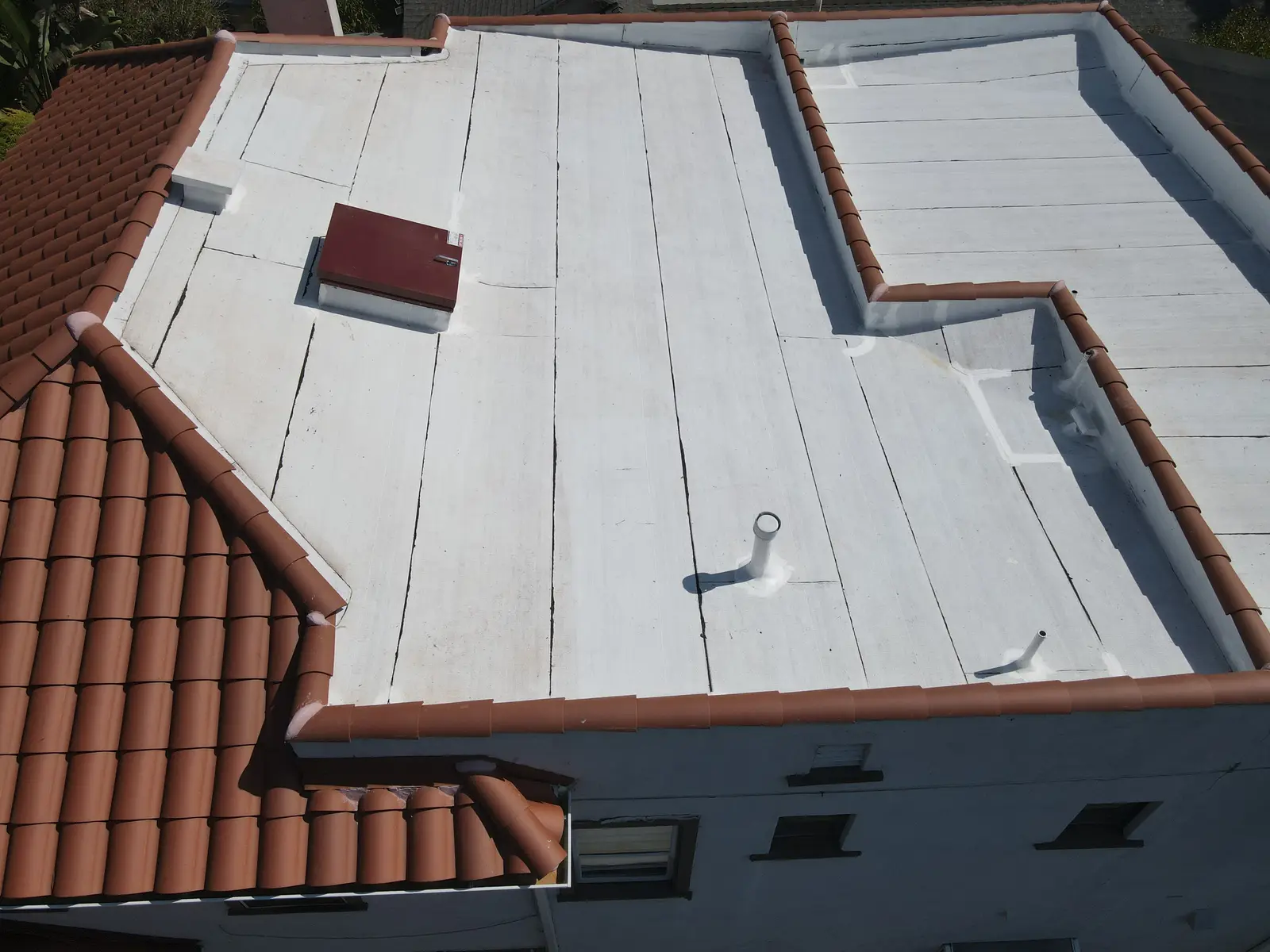 Reflective white flat roof with a roof hatch and vent pipe beside the clay tile slope