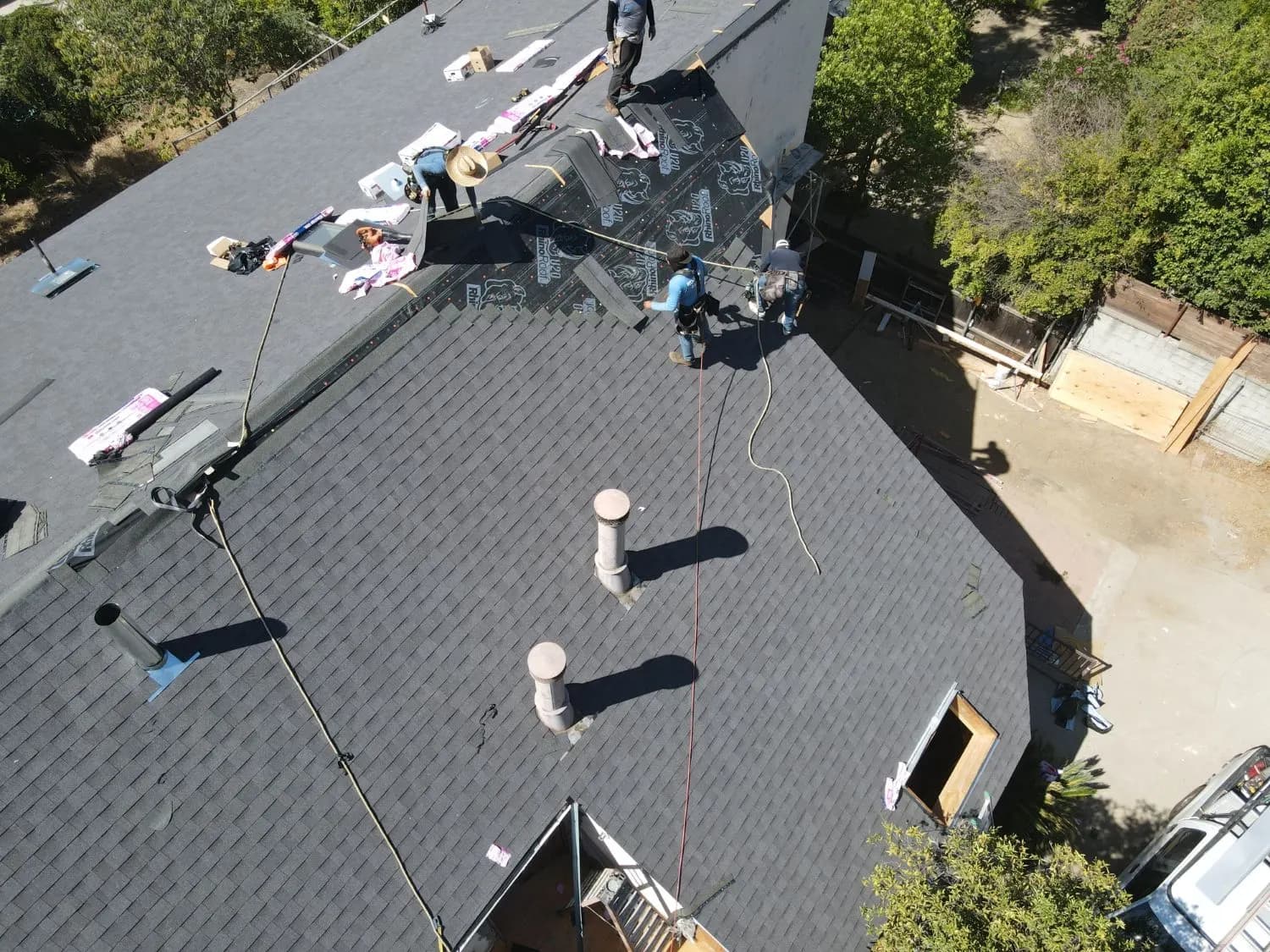 Roofers installing felt underlayment during a shingle roof installation, with materials staged on the roof